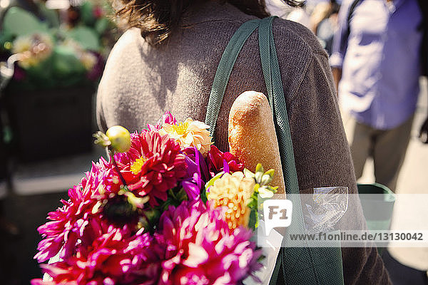 Mitschnitt einer Frau  die auf dem Markt Blumen und Brot im Portemonnaie trägt