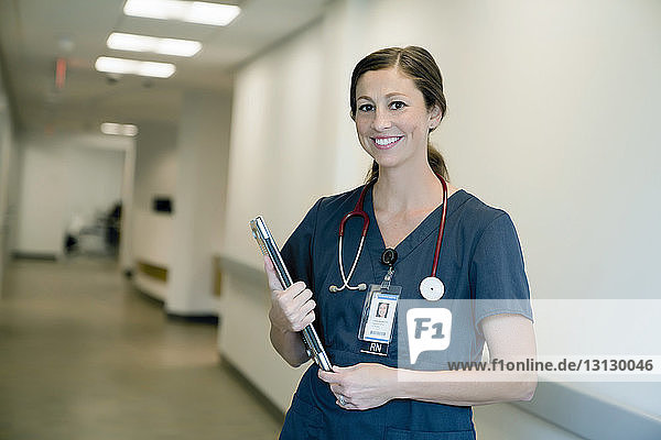 Porträt einer fröhlichen Ärztin  die einen Laptop-Computer hält  während sie in der Krankenhauslobby steht
