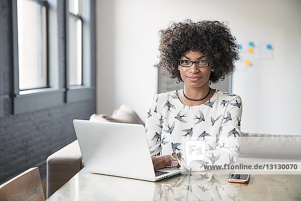Porträt einer selbstbewussten Geschäftsfrau  die im Büro am Schreibtisch sitzt