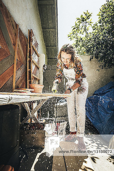 Künstlerin in voller Länge beim Schneiden von Holzbrettern bei der Arbeit im Hinterhof