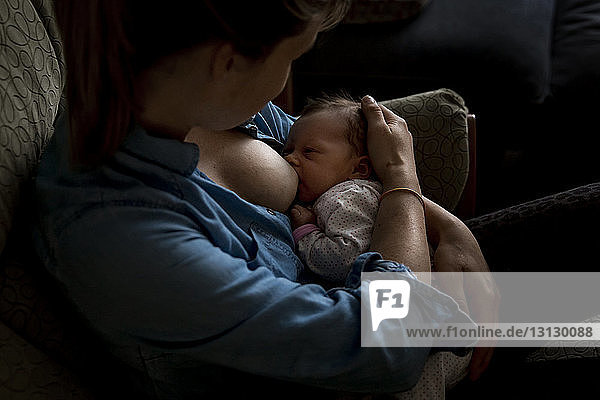 High angle view of mother breastfeeding newborn daughter while sitting on sofa at home