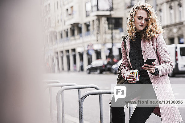 Geschäftsfrau benutzt Smartphone  während sie in der Stadt am Geländer sitzt