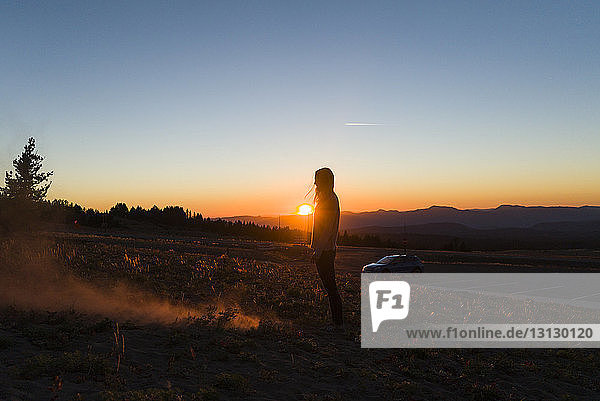 Side view of woman standing on field against sky during sunset