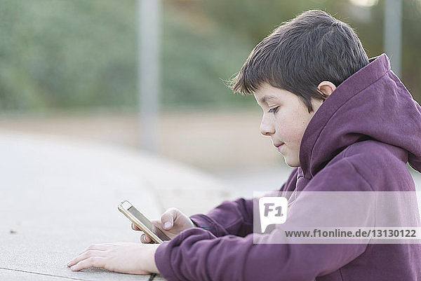 Seitenansicht eines Jungen  der ein Mobiltelefon benutzt  während er im Freien sitzt