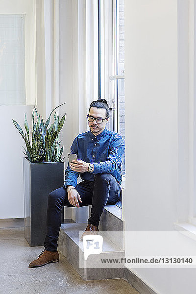 Businessman using mobile phone while sitting at doorway in office