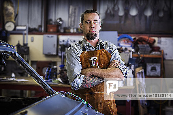 Porträt eines mit verschränkten Armen stehenden Mechanikers in einer Autowerkstatt