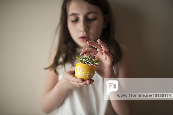 Süßes Mädchen hält Topfpflanze  während es zu Hause an der Wand steht