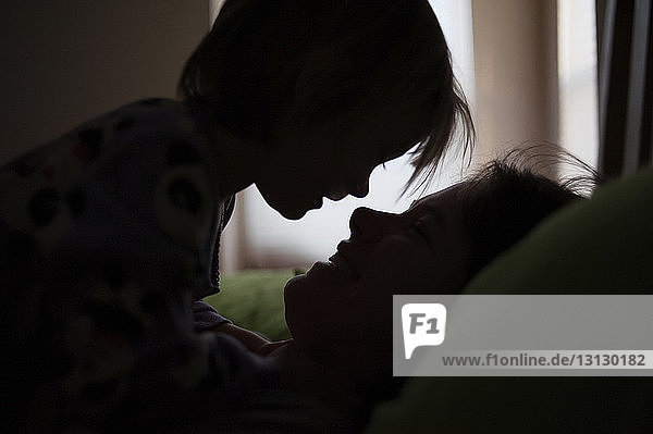 Scherenschnitt Mutter und Tochter schauen einander an  während sie sich zu Hause im Bett entspannen
