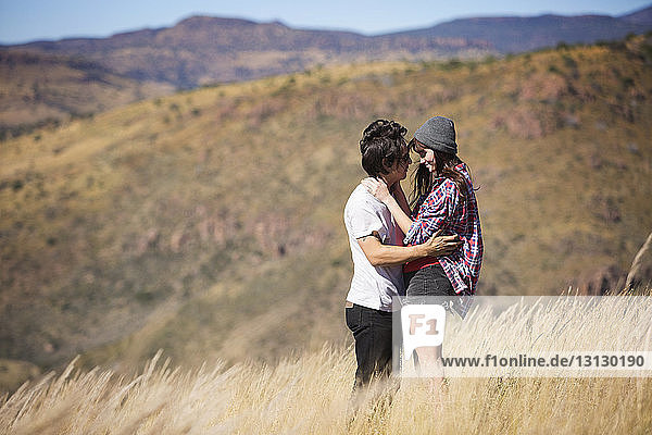 Side view of couple embracing while standing on field