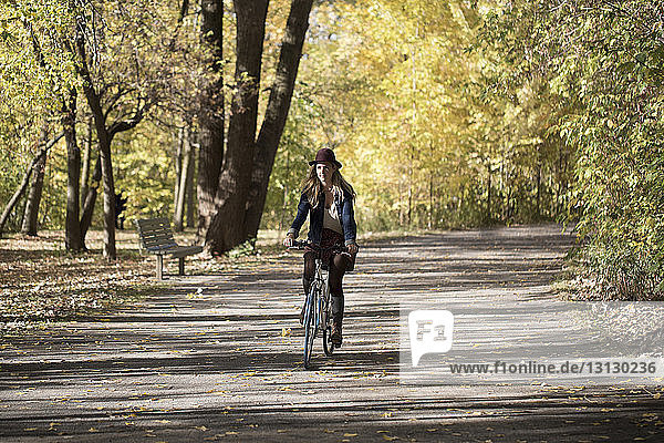 Frau fährt Fahrrad auf Straße zwischen Bäumen