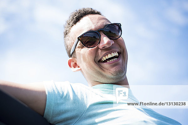 Niedrigwinkel-Porträt eines glücklichen Mannes mit Sonnenbrille  der im Geländewagen gegen den Himmel fährt