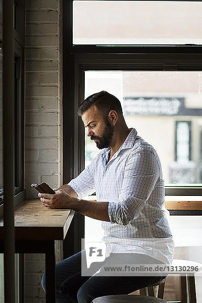 Serious man using phone at table in cafe