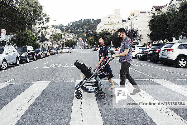 Parents with daughter in baby stroller walking on city street