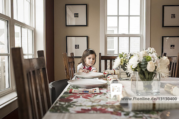 Girl adjusting plate on dining table at home during Christmas