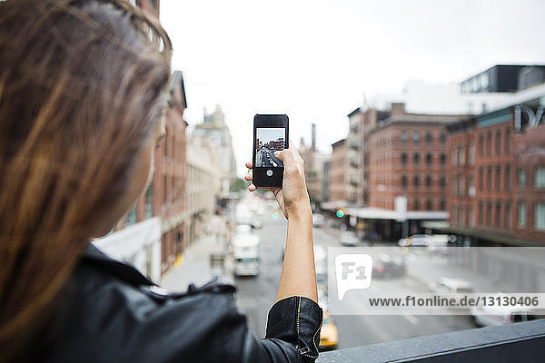 Cropped image of woman photographing city through mobile phone