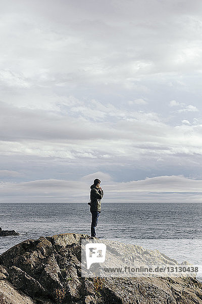 Seitenansicht eines Mannes  der auf einer Felsformation am Meer vor bewölktem Himmel steht