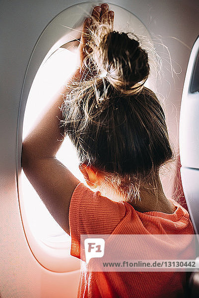 Rückansicht eines Mädchens  das durch ein Flugzeugfenster schaut