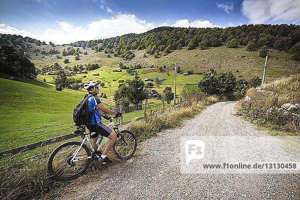 Male athlete with bicycle on dirt road by field