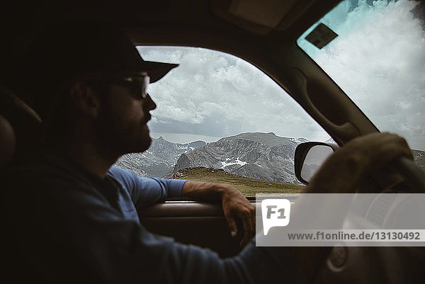 Side view of man driving car on mountain against cloudy sky