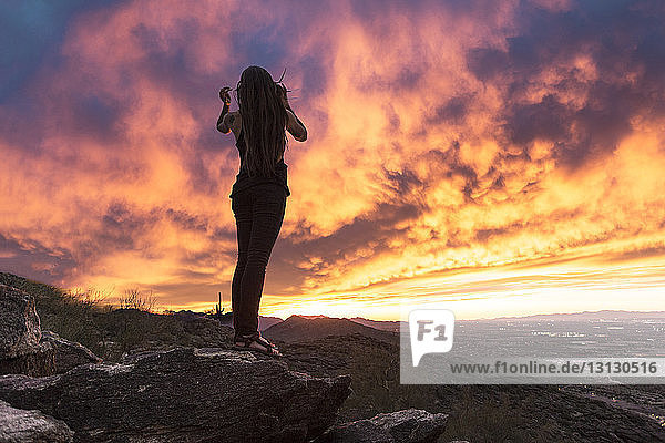 Sorglose Frau in voller Länge auf Fels stehend vor dramatischem Himmel im South Mountain Park