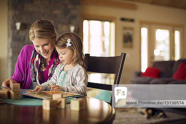 Mother and daughter looking at book on table at home