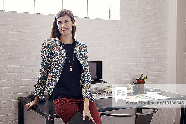 Portrait of smiling confident businesswoman sitting on table against wall