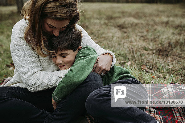 Glückliche Mutter umarmt ihren Sohn  während sie im Park auf einer Decke sitzt