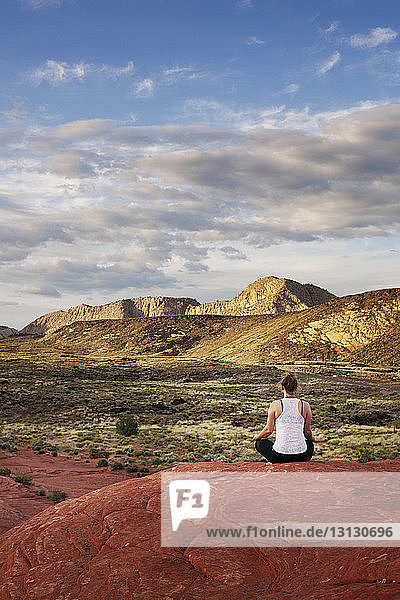Rückansicht einer Frau  die im Berg gegen den Himmel auf Felsen meditiert