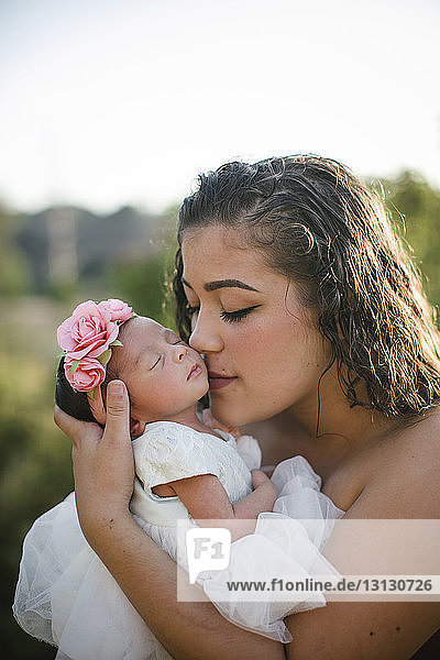 Close-up of mother kissing daughter against sky at park