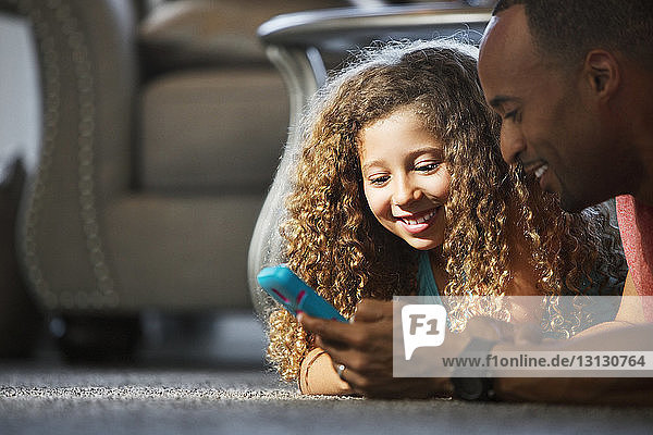 Glücklicher Vater und Tochter spielen Videospiel  während sie zu Hause auf dem Teppich liegen