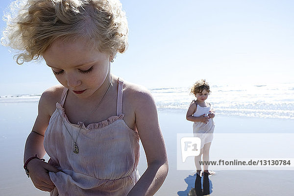 Sisters standing at beach against sky