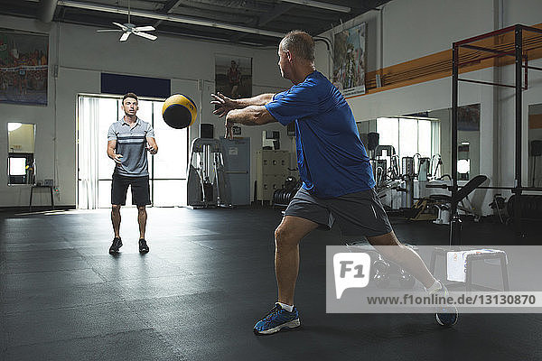 Customer passing fitness ball to trainer while exercising in gym