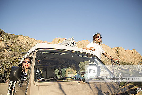 Young couple in mini van enjoying vacation against clear blue sky