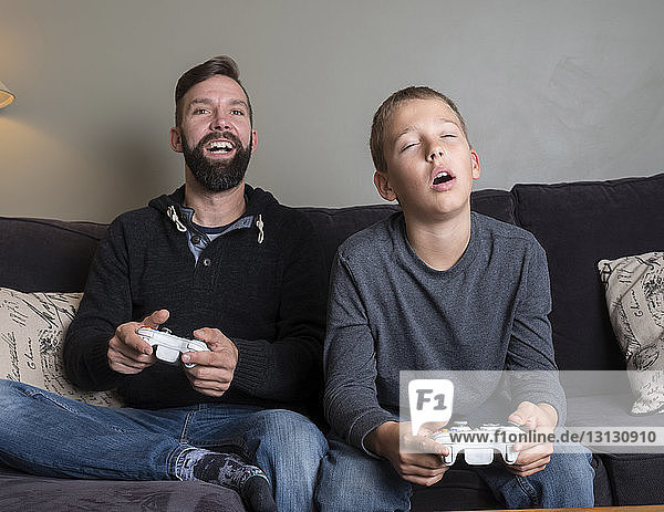Vater mit Sohn spielt Videospiel  während er zu Hause auf dem Sofa sitzt