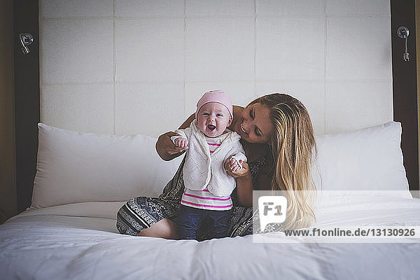 Mother assisting baby to standing on bed at home