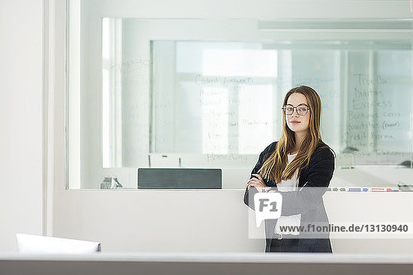 Portrait of confident businesswoman with arms crossed in office seen through window