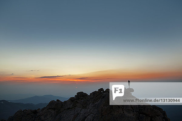 Distant view of man standing on mountain against sky during sunset