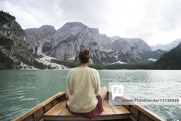 Rear view of woman sitting in boat on river amidst mountain against sky