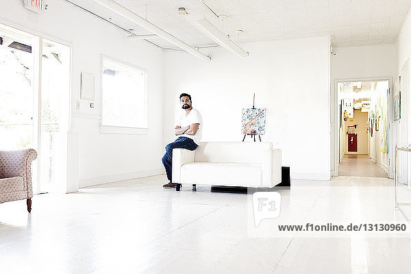 Confident artist sitting on handrest of sofa in art studio