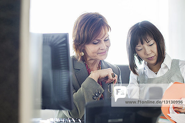 Businesswomen reading document while sitting at office desk