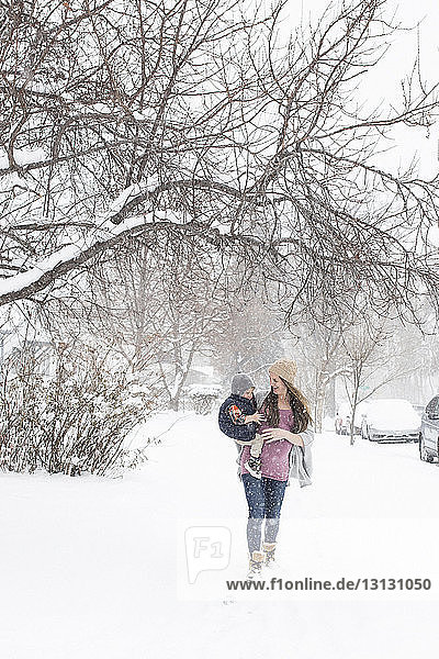 Pregnant mother carrying son while walking on snowy field in city during snowfall