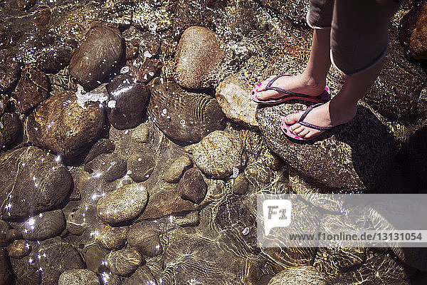 Niedrige Sektion eines Mädchens  das an einem sonnigen Tag auf einem Felsen am Strand steht