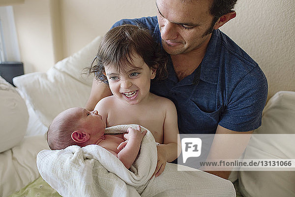 Cheerful sister playing with newborn brother by father at home