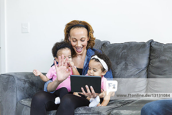 Happy mother and daughters video conferencing on tablet computer