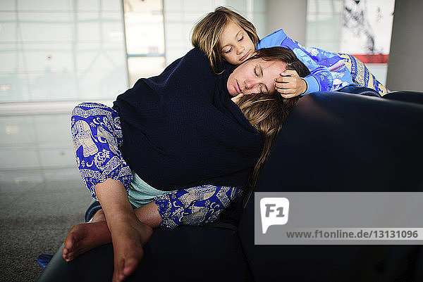 Girl looking at mother sleeping with daughter while sitting on sofa