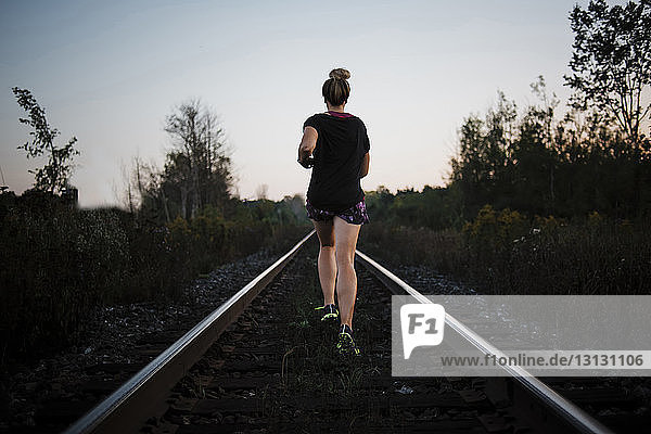 Rear view of woman jogging on railroad track against sky during dusk