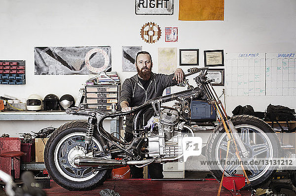 Portrait of confident mechanic standing with motorcycle at auto repair shop