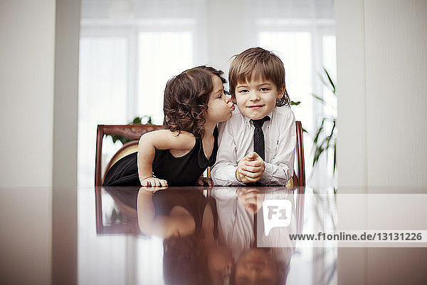 Cute girl kissing brother while sitting at table