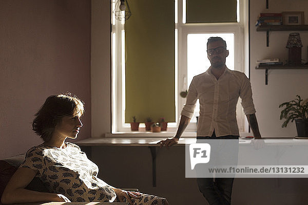 PRegnant woman sitting while man standing in background at home