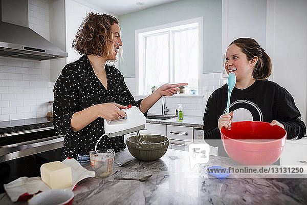 Mother guiding daughter in preparing food on kitchen island at home